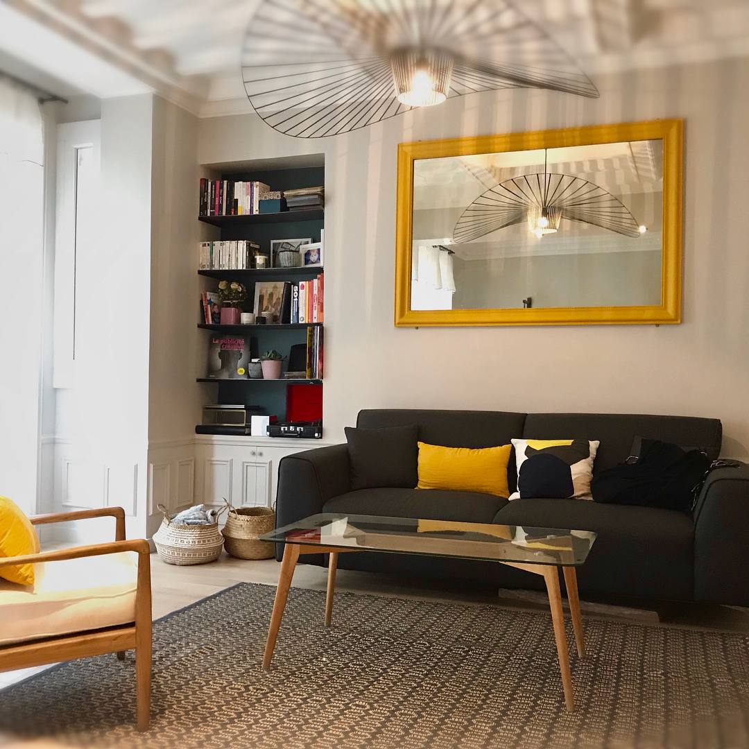 Salon avec bibliothèque sur mesure, miroir jaune et canapé noir - réalisation Atelier 2C